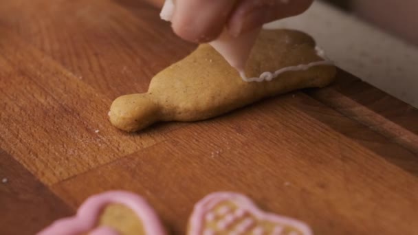 Vrouw versiert een peperkoek in de vorm van een belletje op het houten bureau met glazuur. Kersttraditie. — Stockvideo