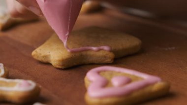 Kadın, ahşap masanın üzerindeki ev şeklinde zencefilli ekmeği kremayla süslüyor. Noel geleneği. 