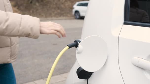 Vrouw komt naar het elektrische voertuig en ontkoppelde voedingskabel op te laden in de straat op laadpunt — Stockvideo