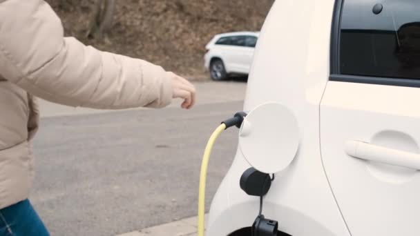 Mulher chegando ao veículo elétrico e desligando o cabo de alimentação para carregar na rua no ponto de carregamento — Vídeo de Stock