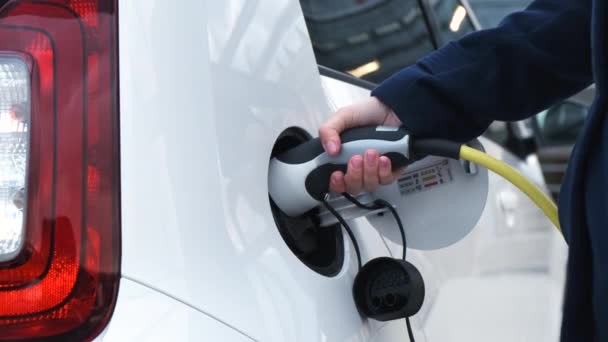 Cerca de la mano de la mujer saca el cable de alimentación del coche eléctrico. — Vídeo de stock