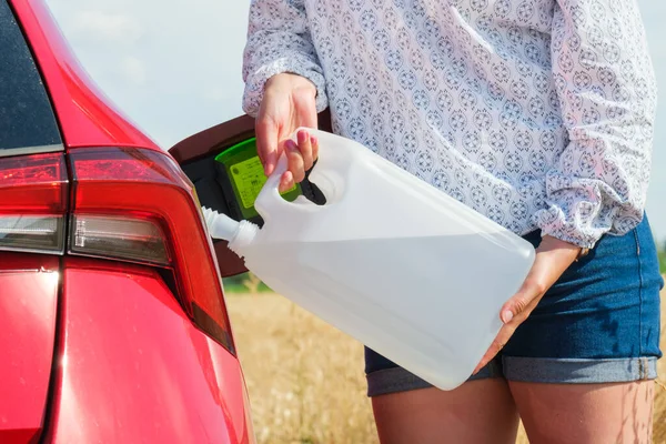Fechar a mulher enchendo o carro vermelho com combustível ou um fluido do motor diesel da lata no campo. — Fotografia de Stock
