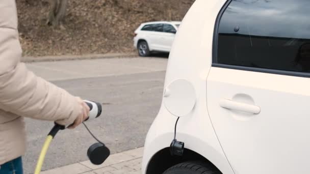 Nő jön az elektromos jármű és dugja be tápegység kábel tölteni az utcán töltőponton — Stock videók