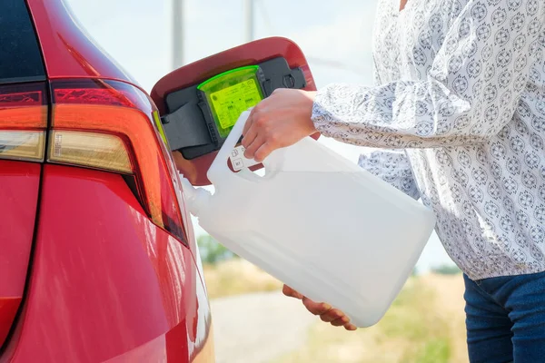 Fechar a mulher enchendo o carro vermelho com combustível ou um fluido do motor diesel da lata no campo. — Fotografia de Stock