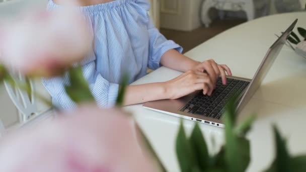Femme freelance tapant du texte sur le clavier de l'ordinateur portable. Travailler dans un intérieur moderne avec des pivoines roses et des roses jaunes. Lieu de travail romantique. — Video