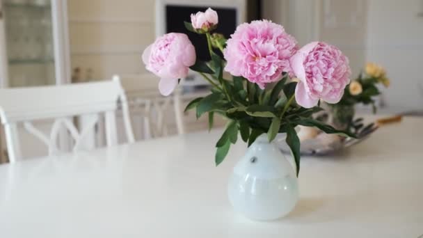 現代の明るいインテリアの大きなテーブルの上に白い花瓶にピンクの牡丹と黄色のバラ — ストック動画