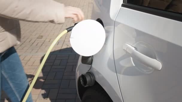 Женщина, приходящая к электрическому автомобилю и отключение кабеля питания для зарядки на улице в точке зарядки — стоковое видео