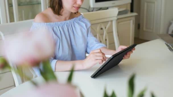 Vrouw die met potlood aan de tablet werkt in het licht moderne interieur. Freelancer of interieurontwerper zit in de woonkamer en tekent. — Stockvideo