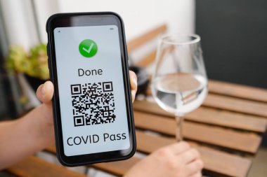 Kafede oturan kadın, cep telefonunda QR kodu bulunan Covid pasaport ya da dijital sağlık pasaportu gösteriyor