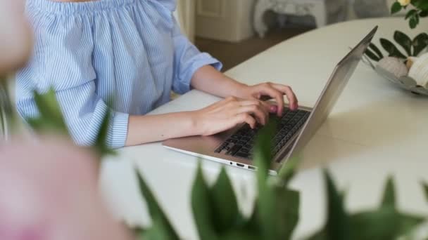 Femme freelance tapant du texte sur le clavier de l'ordinateur portable. Travailler dans un intérieur moderne avec des pivoines roses et des roses jaunes. Lieu de travail romantique. — Video