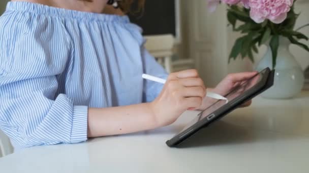 Žena pracující na tabletu pomocí tužky ve světle moderním interiéru. Freelancer nebo interiérový designér sedí v obývacím pokoji a kreslí. — Stock video