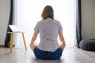 Genç bir kadın oturma odasında meditasyon yapıyor ya da yoga yapıyor. İnternetteki eğitim uygulaması tableti kullanıyor. 