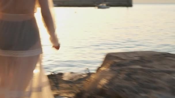 Una donna in abito bianco e corpo nero corre lungo il molo verso il mare al tramonto o al tramonto. Godetevi la splendida vista e relax — Video Stock
