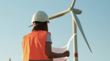 Elinde kağıt bir proje olan rüzgar türbinlerinden oluşan bir mühendis sahadaki yel değirmenine bakıyor. Yeşil eko elektrik üretimi ve yenilenebilir enerji. 