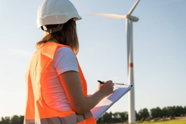 Kadın bakım mühendisi rüzgar türbinleri ve yel değirmenlerinin çalışmalarını kontrol ediyor. Yenilenebilir enerji teknolojisi. Yeşil elektrik üretimi. 