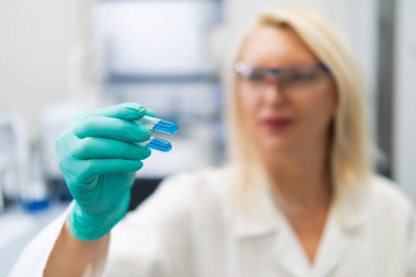Blonde woman in lab coat studying blue liquid in test tube in chemistry lab.
