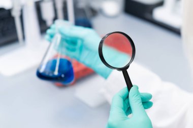 Laboratuvar çalışanlarının elleri matarayı tutsun ve büyüteçle sıvı çözeltiyi incelesin.