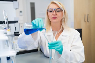 Kadın bilim adamı, laboratuvardaki cam bacadan kimyasal çözeltiyi dikkatlice döküyor. Kesin bilimsel araştırma, kimya deneyi ve modern laboratuvar teknikleri kavramı.