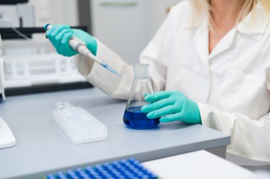 Laboratuvardaki sarışın kadın bilim adamı cam şişede kimyasal solüsyon hazırlamak için pipeti dikkatlice kullanıyor. Laboratuvar araştırması kavramı.