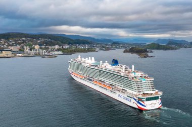 ALESUND, NORWay - 12 Mayıs 2025: Alesund kasabası yakınlarındaki dağ siluetinde sakin fiyort sularında seyir gemisi. Çok sayıda güverte ve renkli cankurtaran sandalları bulutlu gökyüzü altında