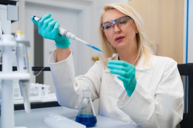 Laboratuvarda sarışın kadın kimyager test tüpünde çözeltiyi pipetle hazırlıyor..