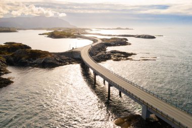 Dönen Atlantik okyanus yolu deniz suyu boyunca küçük kayalık adaları birbirine bağlar. Bulutlu gökyüzü altında Norveç takımadalarından geçen resim gibi bir rota