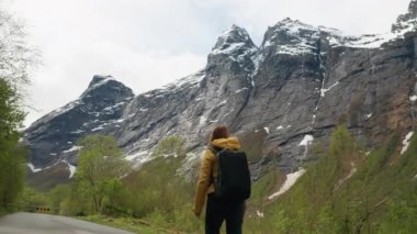 Norveç 'te sırt çantasıyla dağ yolunda yürüyen aktif genç bir kadın. Kayalık uçurumları ve vadileri olan güzel İskandinav manzarası. Kuzey doğasında macera, seyahat ve özgürlük kavramı.