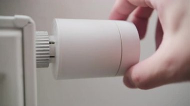 Radyatör termostatını dönen adam, içeride ısıtma seviyesini düşürmek için iklim kontrolü yapıyor..