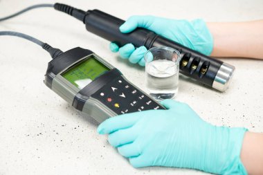 Koruyucu eldivenli kadın elleri pH ölçer ile su pH 'ını ölçer..