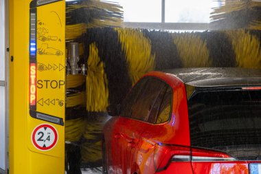 Dönen fırçalar ve su jetleri ile kırmızı bir aracı otomatik olarak yıkama.