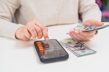 Mali işlerle ilgilenen, dolar sayan ve akıllı telefon hesap makinesindeki harcamaları kontrol eden bir kadın. Para denetimi ve gelir planlaması kavramı.