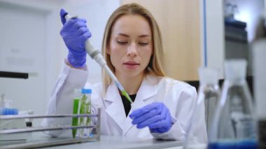 Laboratuvar önlüklü kadın pipetle bitki solüsyonu naklediyor. Biyoteknoloji, destek geliştirme ve kimyasal analiz teması.