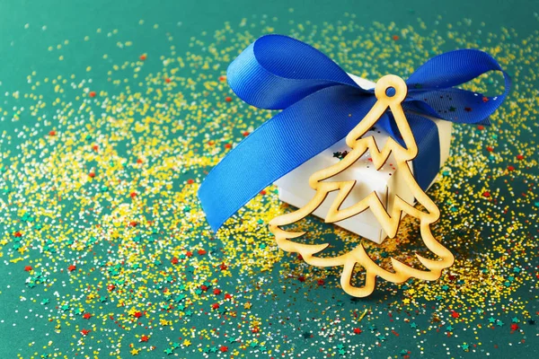 Yeşil arka planda Noel ağacı olan beyaz hediye kutusu. Şenlikli konfeti büyülü bir atmosfer ekler..