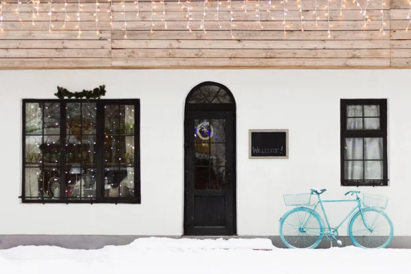 Dükkanın yakınına park edilmiş mavi bir klasik bisiklet. Kapılar, pencereler ve çatı Noel arifesinde çelenk ve çelenkle süslenir. Duvarında selam yazan bir pano. Minimalizm.