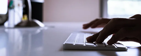 Silhouetted image of a man typing on the wireless keyboard close up with copyspace.