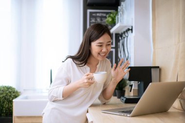 Neşeli Asyalı kadın sabahları bir fincan kahve içip internette sosyal medya aramaktan hoşlanıyor. İş kadını laptopta e-postayı kontrol ediyor ve sabahları kahve içiyor.
