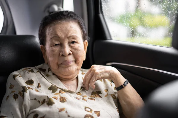 Very old Asian passenger woman age between 80 - 90 years old traveling by the car while raining. Cheerful retired woman in a private car portrait with copy space. Wellness and wellbeing in old people