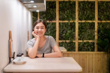 Güzel Asyalı kadın, küçük restoranın menüsüne bakıyor. Neşeli Asyalı kadın restoranda yemek bekliyor..