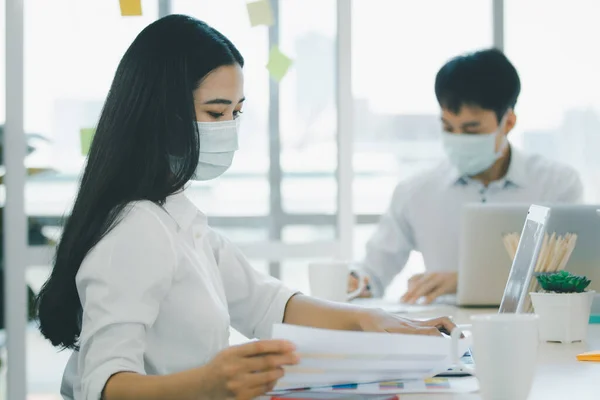 Group of senior businesspeople with hygiene protective face mask in meeting and discussing in the office, enterprise business meeting. Serious staff meeting in the workplace.