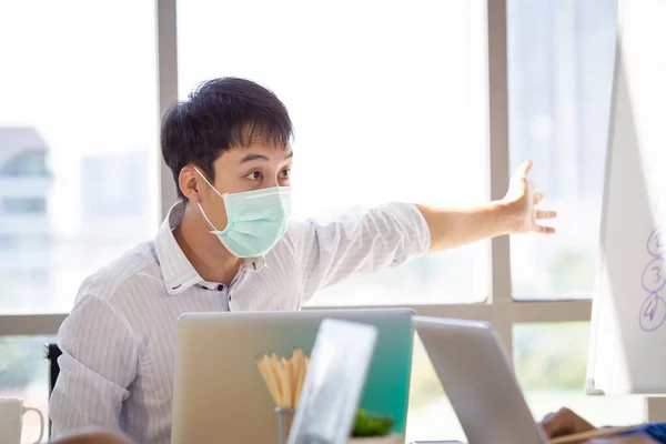 Group of senior businesspeople with hygiene protective face mask in meeting and discussing in the office, enterprise business meeting. Serious staff meeting in the workplace.
