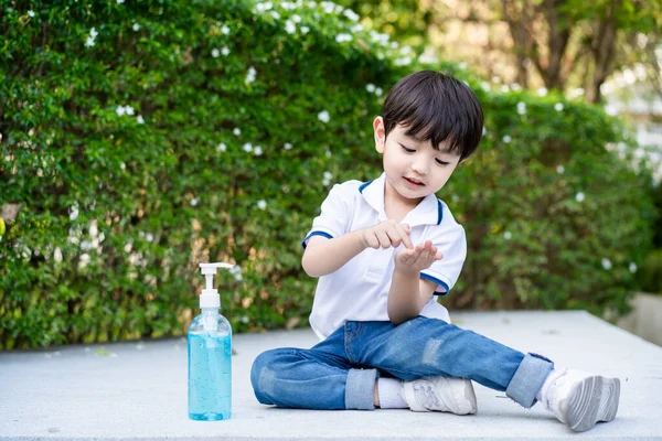 Asyalı mutlu çocuk parkta dinlenirken sıvı el dezenfektanı ya da alkol jeli kullanıyor ve uyguluyor. El dezenfektanı kullanarak el temizleme ve salgın veya virüsü önleme. COVID19 'dan uzak dur.
