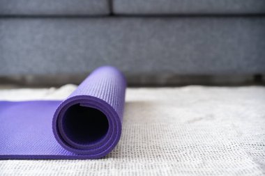 Oturma odasında yerde yuvarlanmış mor yoga egzersiz paspası. Kopyalama alanı ile yakın çekim. Kapalı alanda çalışma etkinliği konsepti. Yuvarlanan Mor Yoga halısı. Yaklaş..