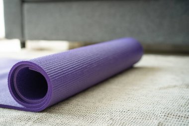 Oturma odasında yerde yuvarlanmış mor yoga egzersiz paspası. Kopyalama alanı ile yakın çekim. Kapalı alanda çalışma etkinliği konsepti. Yuvarlanan Mor Yoga halısı. Yaklaş..