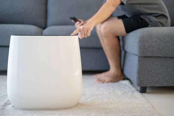 Unrecognizable Asian young man using and controlling a modern air purifier via smartphone, modern household devices in the IOT - internet of thing era. Man turn on air purifier through smartphone.