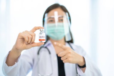 Yüz maskesi ve yüz kalkanı olan Asyalı kadın doktor Coronavirus 2019-nCoV ya da COVID-19 aşısını kopyalama alanına yakın gösteriyor. Coronavirus aşıyı tedavi eder. Doktor COVID19 aşısını işaret ediyor..