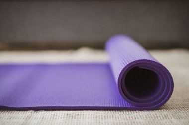 Oturma odasında yerde yuvarlanmış mor yoga egzersiz paspası. Kopyalama alanı ile yakın çekim. Kapalı alanda çalışma etkinliği konsepti. Yuvarlanan Mor Yoga halısı. Yaklaş..