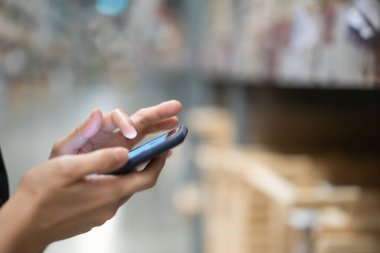 Unrecognizable woman using a smartphone with blurred copyspace background. Girl searching for a merchandise in a store by using application on smartphone.