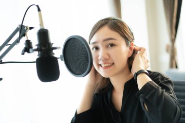 Mutlu Asyalı kadın evinde podcast stüdyosu için bir oturma odası kuruyor, evinde bir podcast ve online radyo istasyonu düzenleyen bir kadın. Profesyonel genç podcaster mikrofon aracılığıyla konuşuyor..