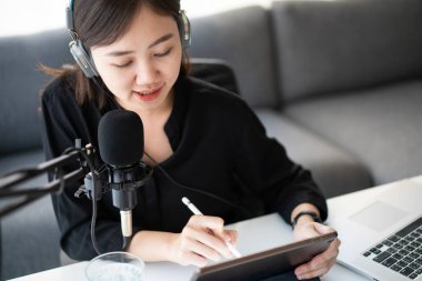 Güzel ve yakışıklı Asyalı kadın podcast kanalını düzenliyor. İş kadını internetteki yayını için bilgisayarından ve tabletinden canlı yayın yapıyor. Modern çalışma tarzı