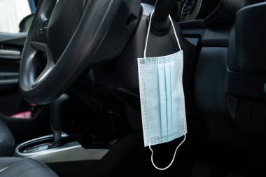 Tıbbi yüz maskesi, modern bir araca takılan far kumandasında asılı. COVID-19 Coronavirus gribi - grip önleme ve karantina konsepti. Sağlık hizmetleri insanları kavramı.